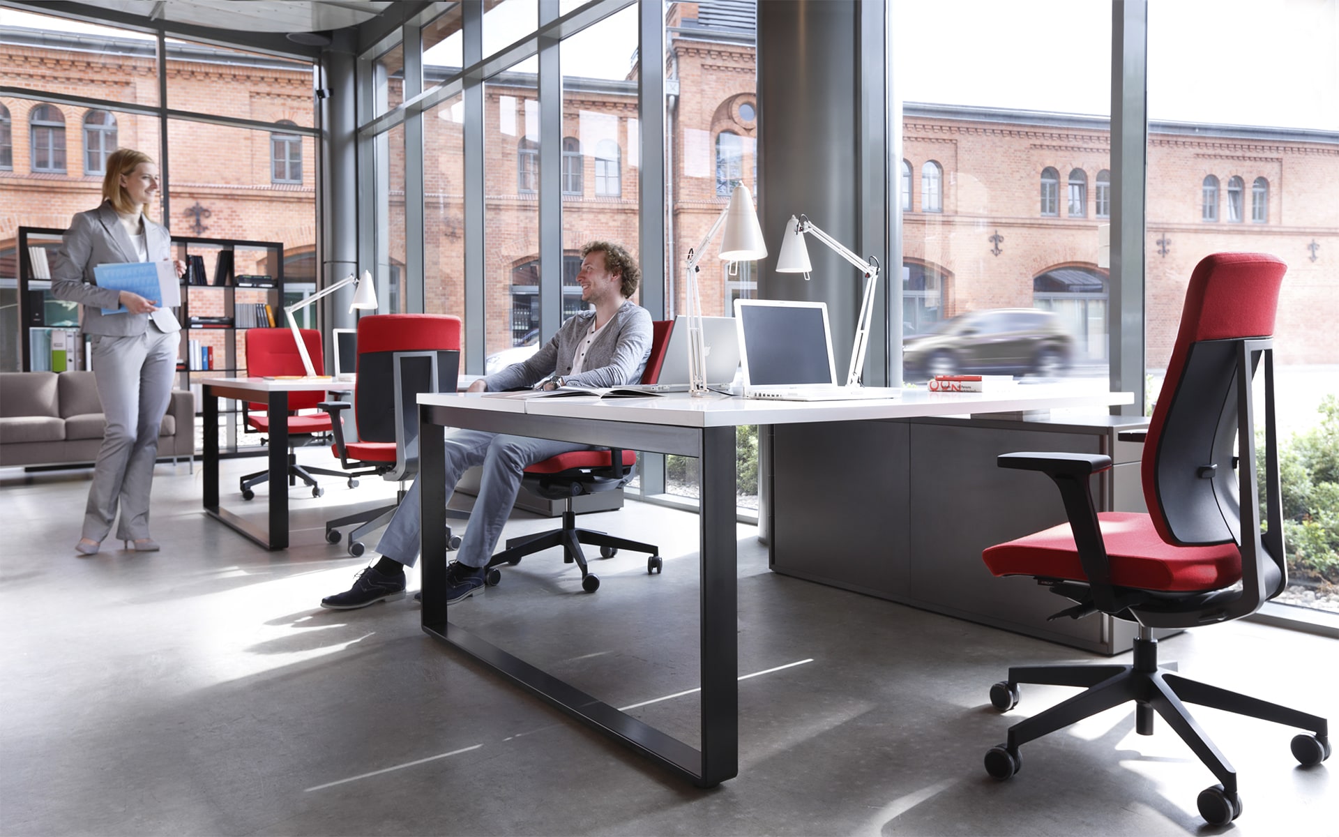 Man and woman at bright workplace that is furnished with red Profim Xenon office chairs by ITO Design