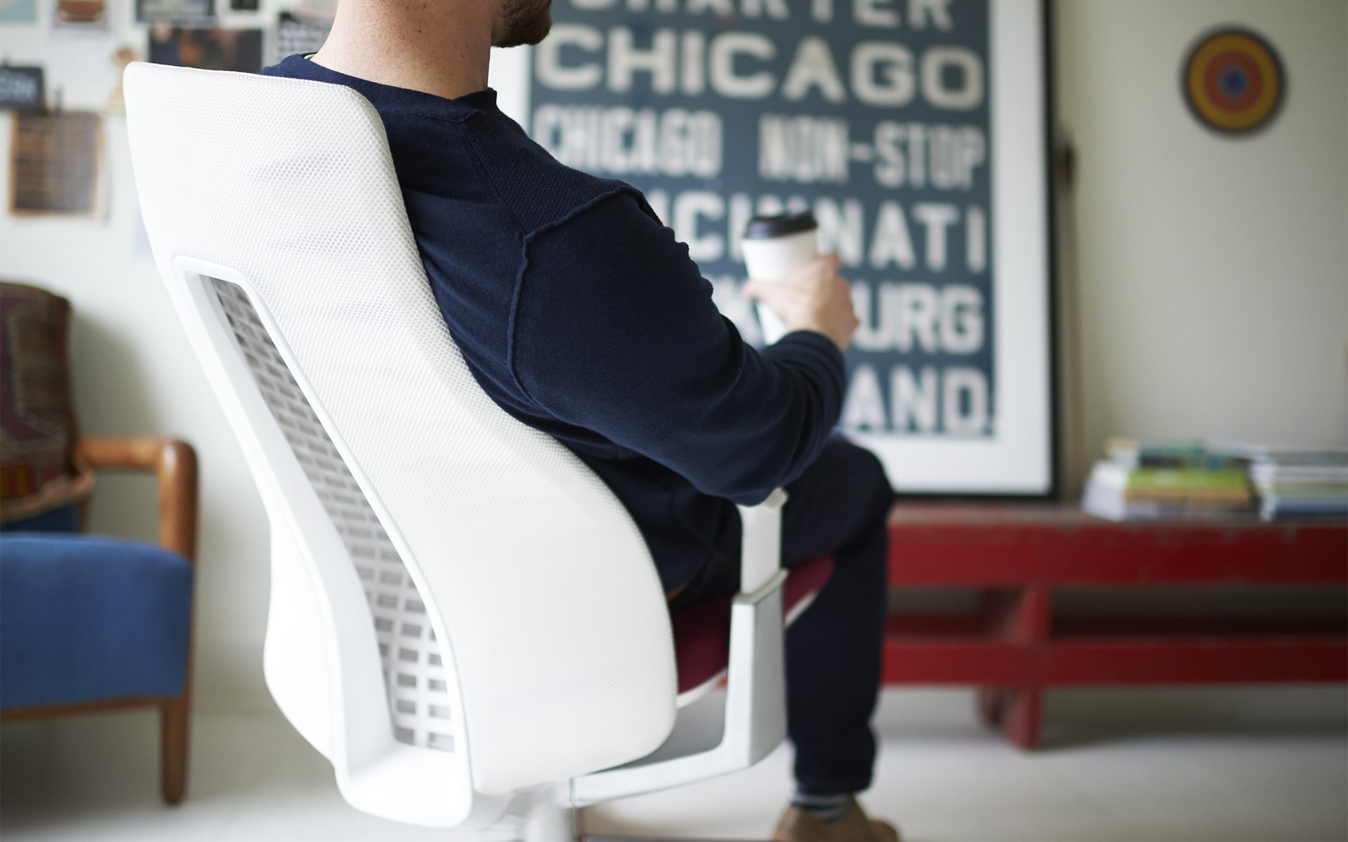 Man with coffee to go sits on Haworth Fern office chair by ITO Design with white backrest