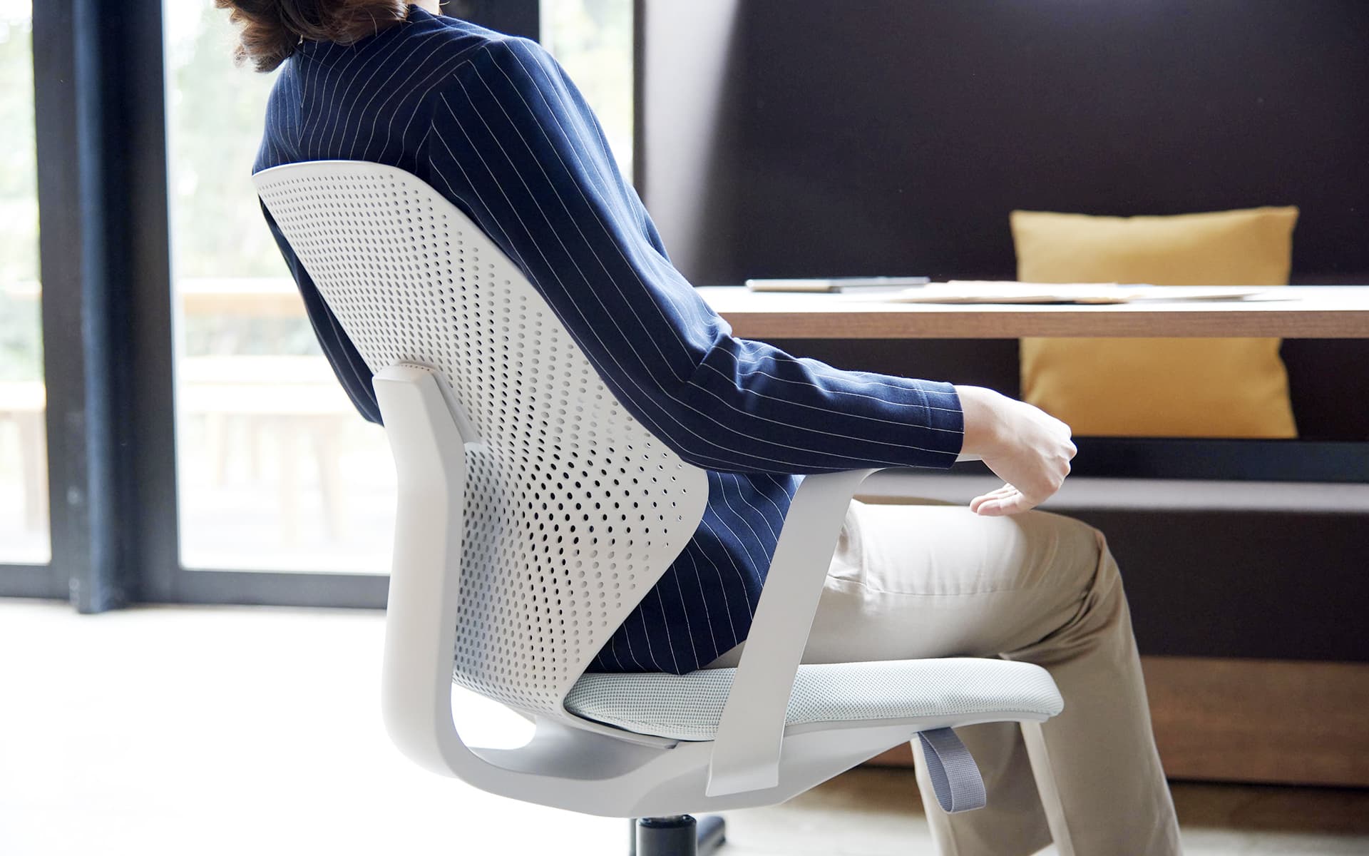 Eine elegant gekleidete Frau sitzt in einem weißen ITOKI QuA Bürostuhl von ITO Design