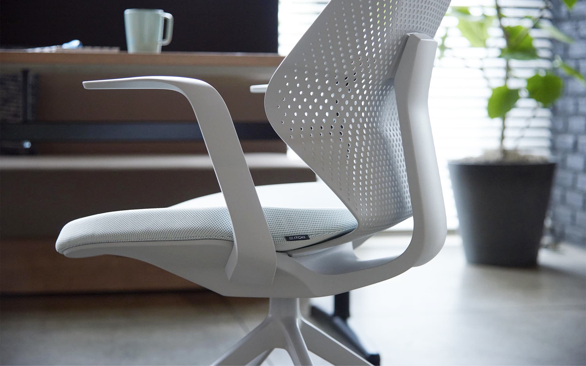 Ein weißer ITOKI QuA Bürostuhl von ITO Design vor einem Naturholz-Schreibtisch mit Tasse