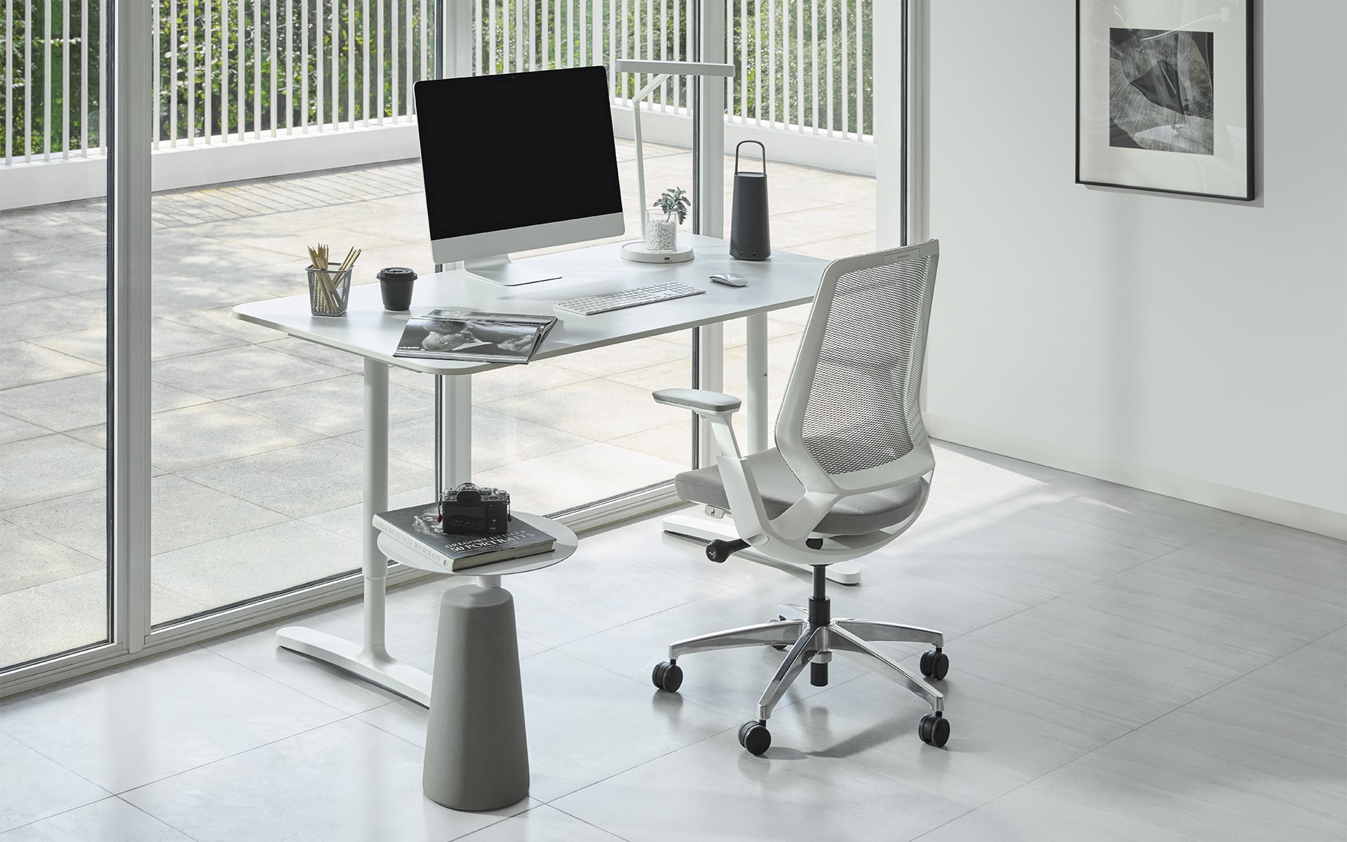 Okamura Abilis office chair by ITO Design with light gray upholstery, light gray mesh backrest and white frame in front of a large window front in a bright room.